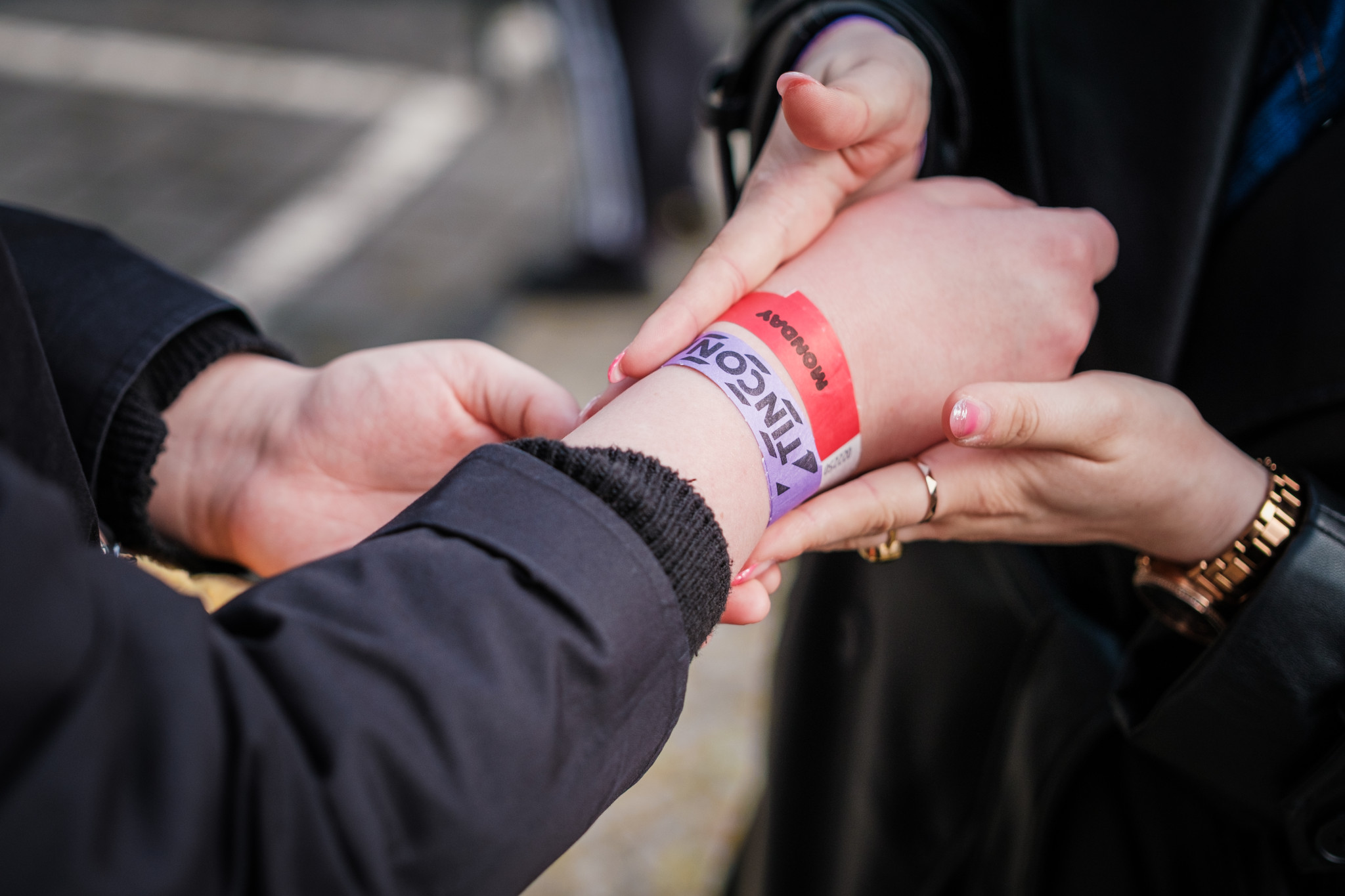 Zwei Hände legen ein TINCON-Papierarmbändchen an einem Arm an